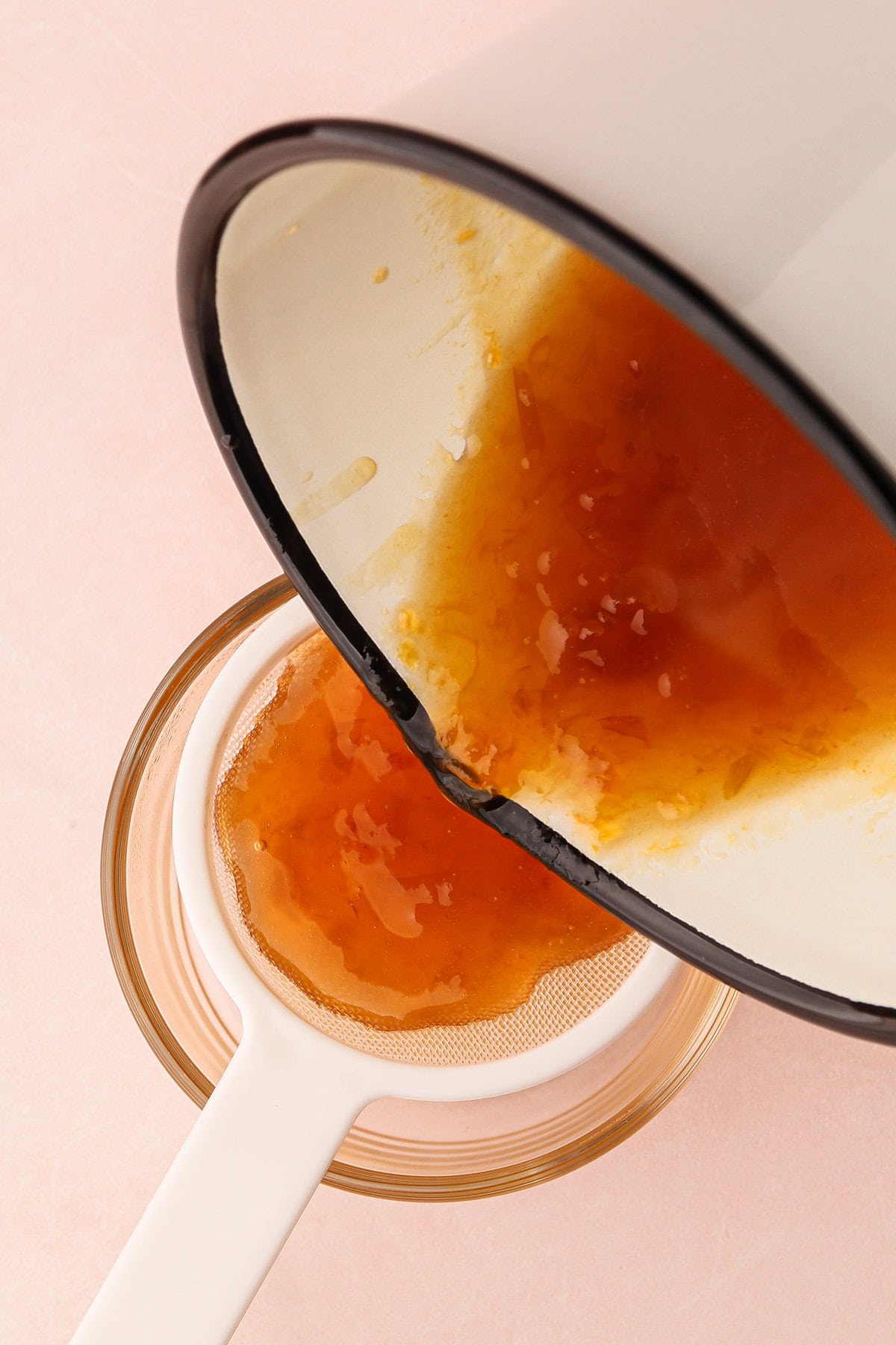 Straining apricot preserves into a bowl to create a smooth fruit tart glaze.