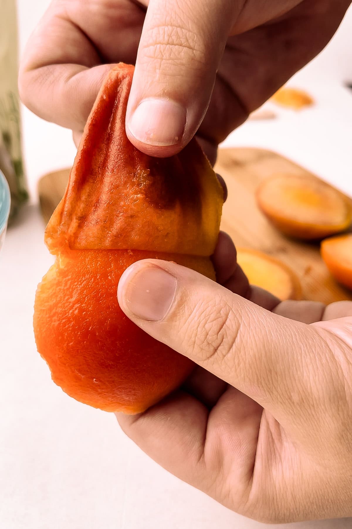 Close-up of a hand peeling a peach, perfect for a peach tarte tatin recipe.