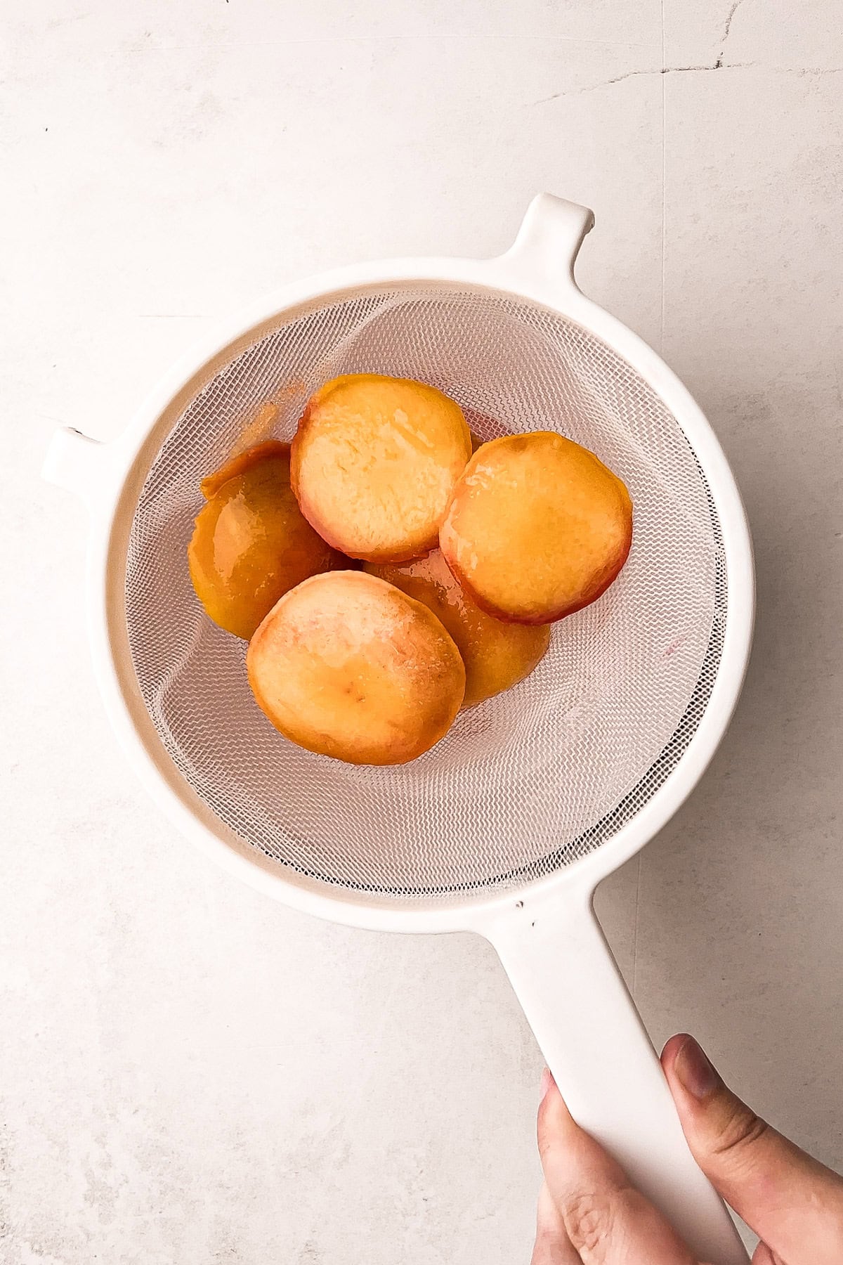 Sliced peaches draining in a mesh strainer, prepared for mini peach tarte tatins.