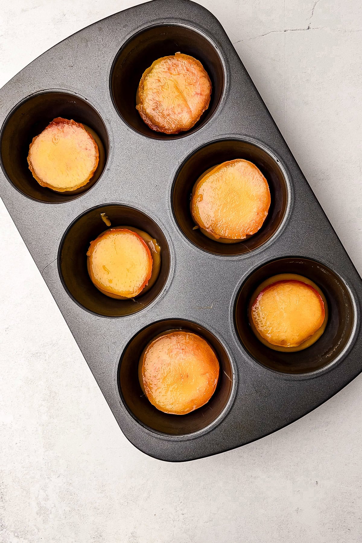 Peaches in caramel sauce in a muffin tin, ready for puff pastry.