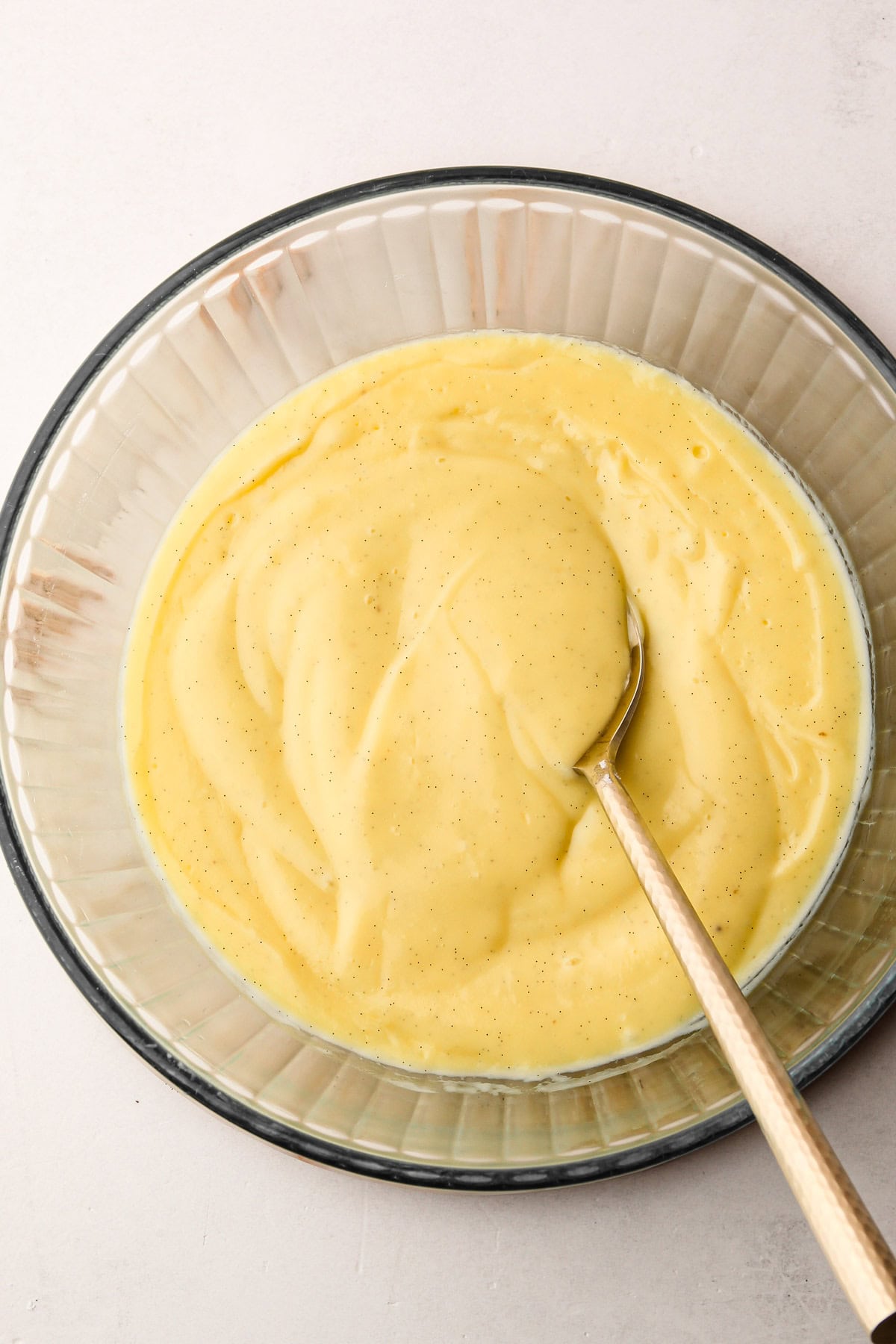 Close-up of the creamy pastry cream texture in a glass bowl with a spoon.