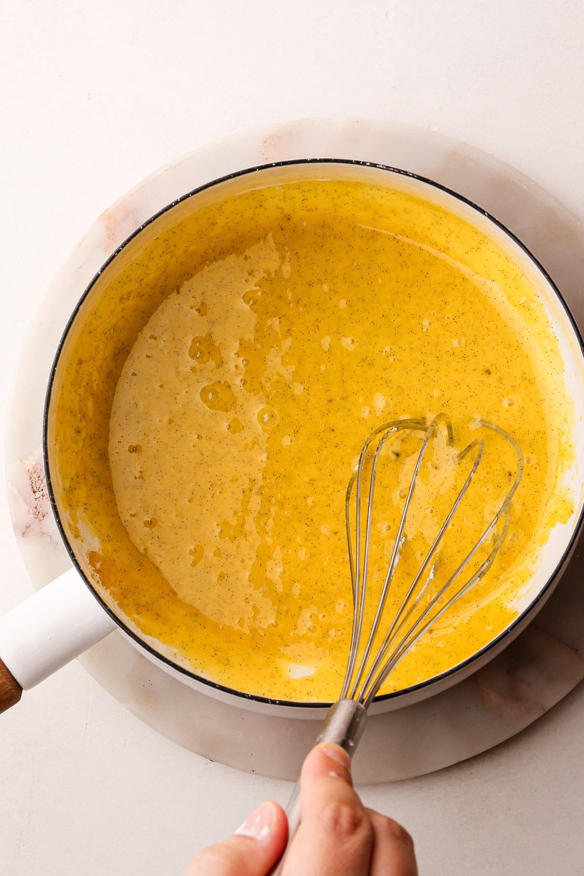 A hand whisking a mixture of eggs and sugar for pastry cream before cooking.