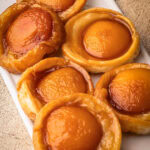 Baked mini peach tarte tatins arranged on a white serving platter.