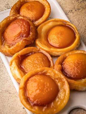 Baked mini peach tarte tatins arranged on a white serving platter.