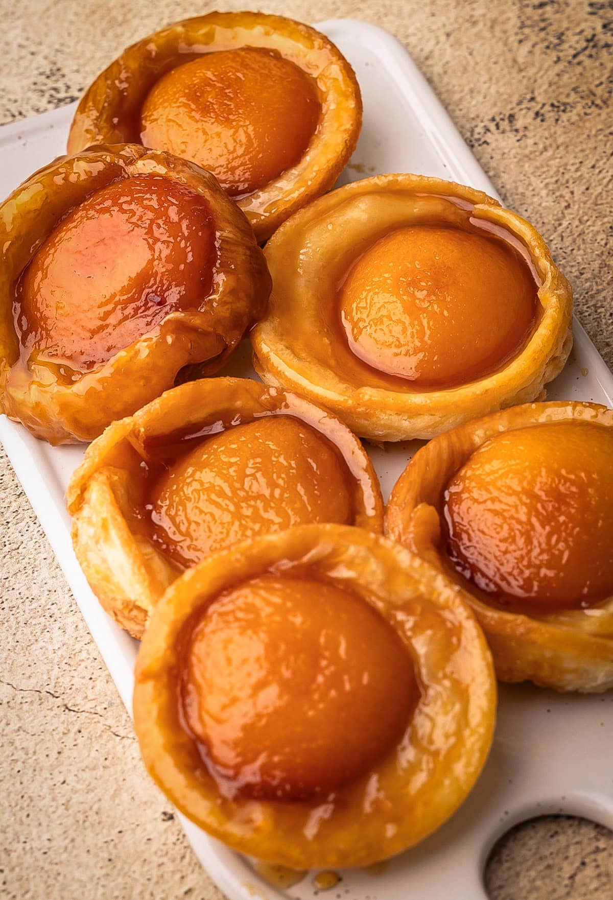 Baked mini peach tarte tatins arranged on a white serving platter.