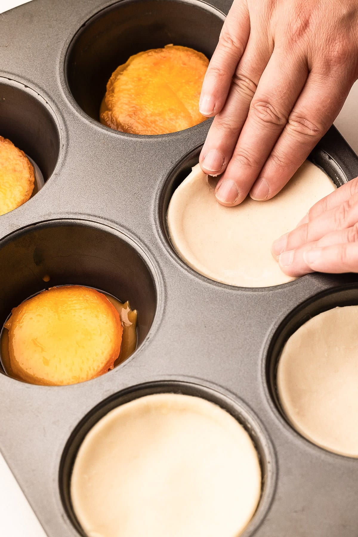 Placing puff pastry over peach halves in a muffin tin, preparing mini peach pastries.