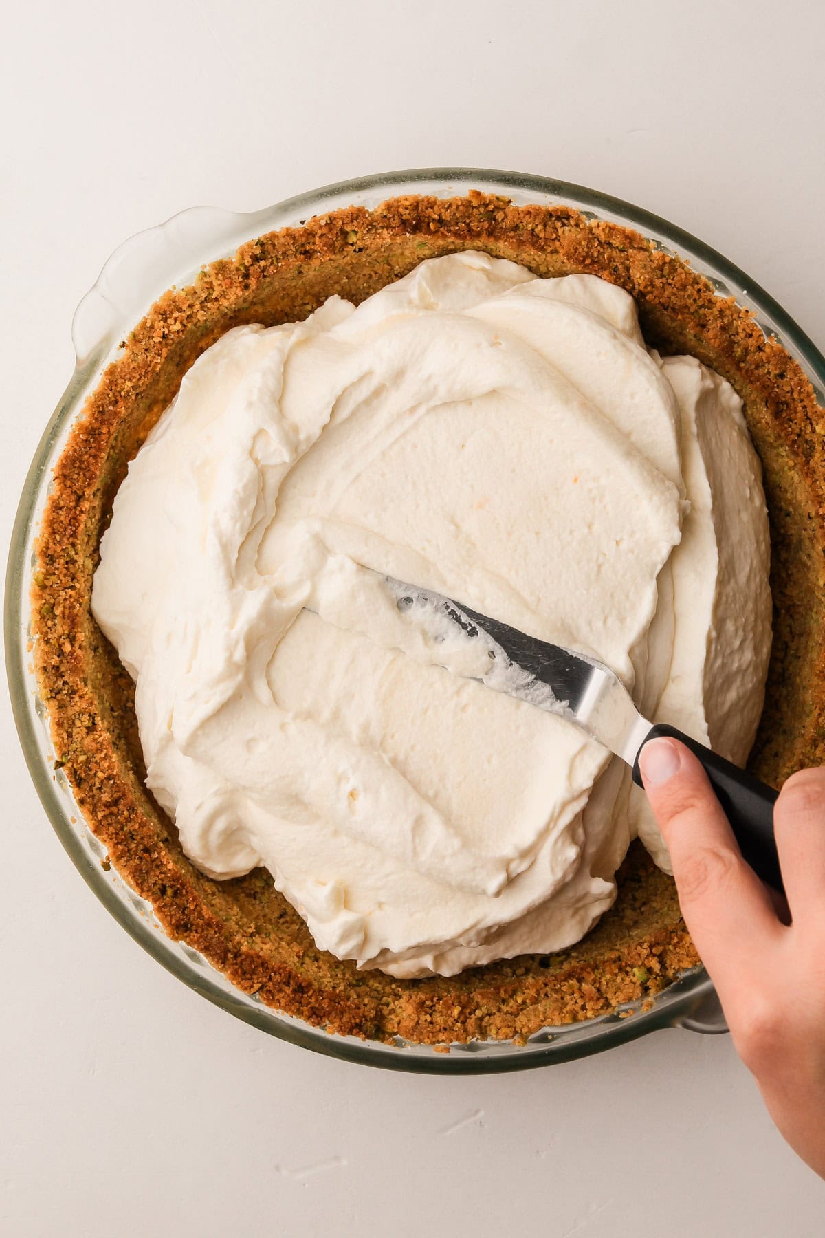 Cannoli pie filling being spread into the prepared crust with an offset spatula.