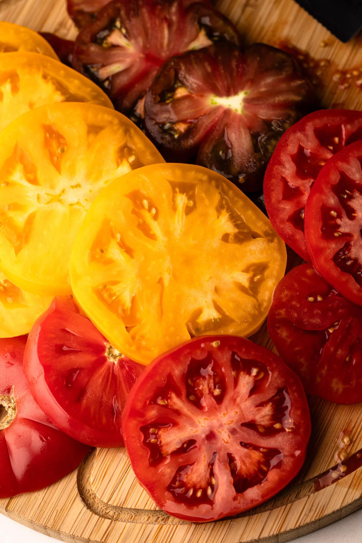 Slices of colorful heirloom tomatoes arranged on a wooden board.