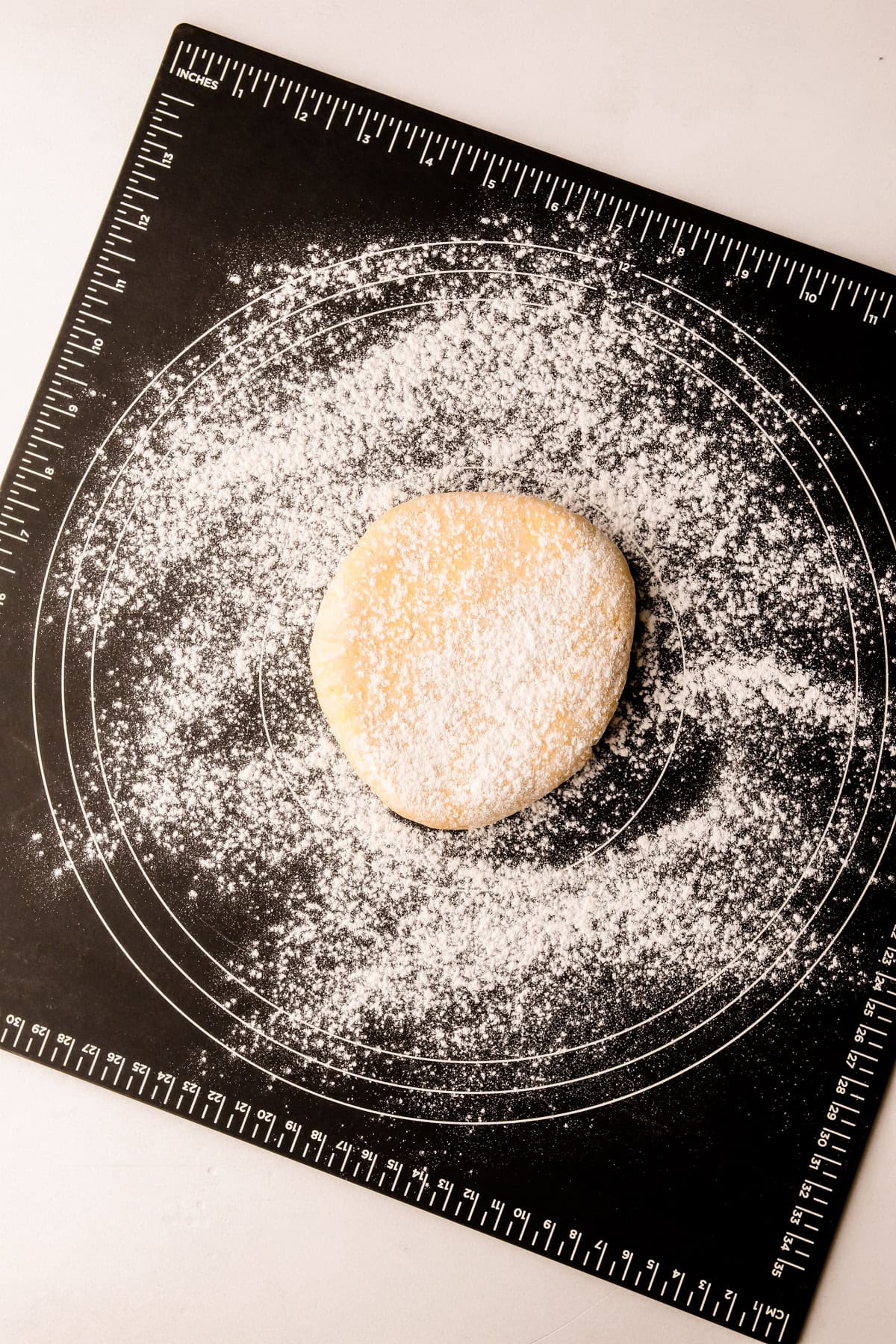 A ball of dough dusted with flour on a black pastry mat.