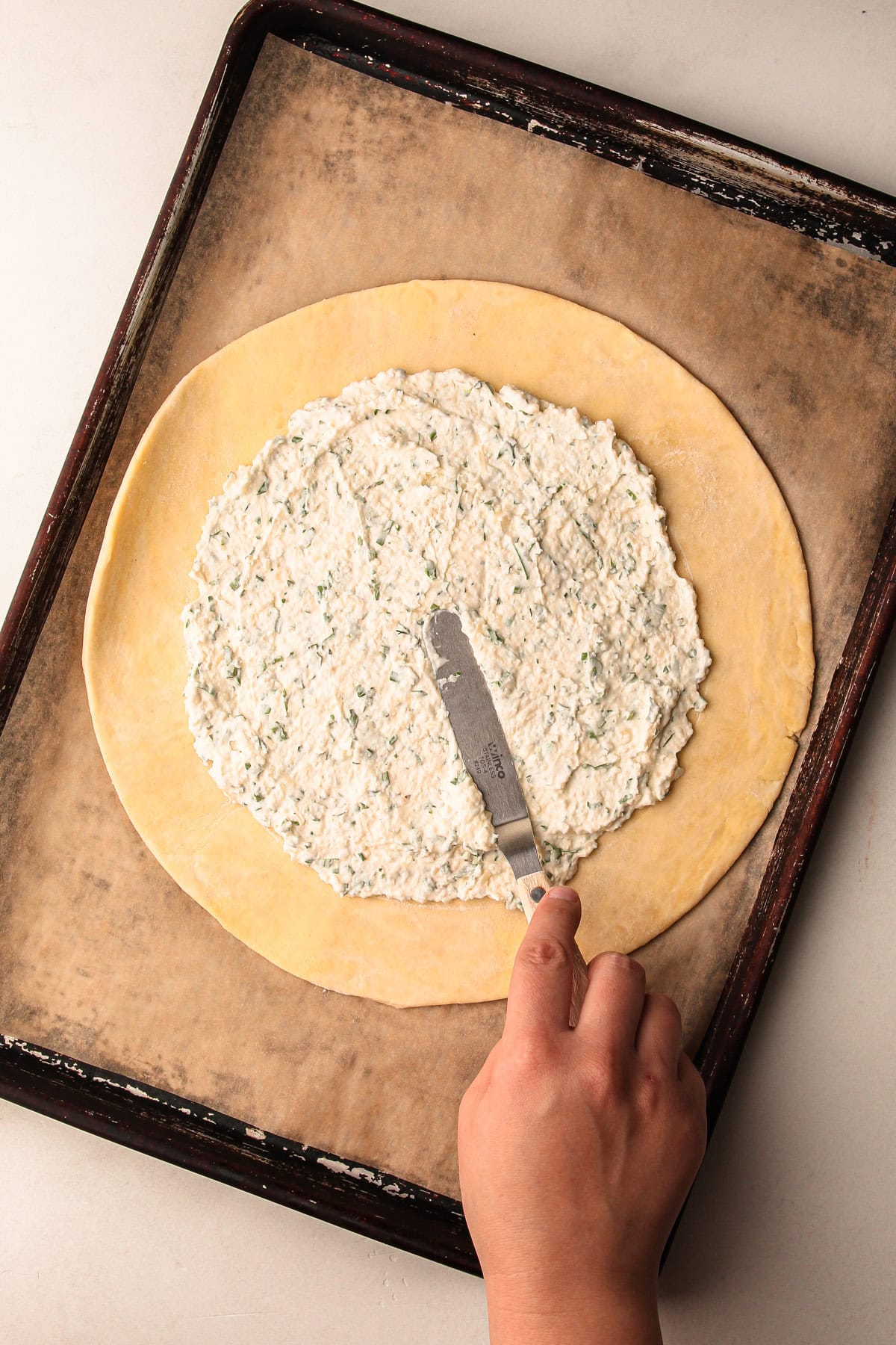 Spreading a crème fraîche and herb mixture on the rolled-out dough.