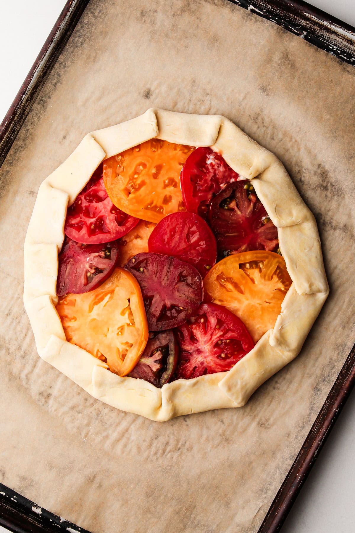 Unbaked galette with heirloom tomatoes arranged on top of the dough with the edges folded over.