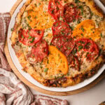 Freshly baked tomato galette with heirloom tomatoes and herbs on a white plate.