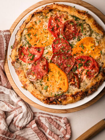 Freshly baked tomato galette with heirloom tomatoes and herbs on a white plate.