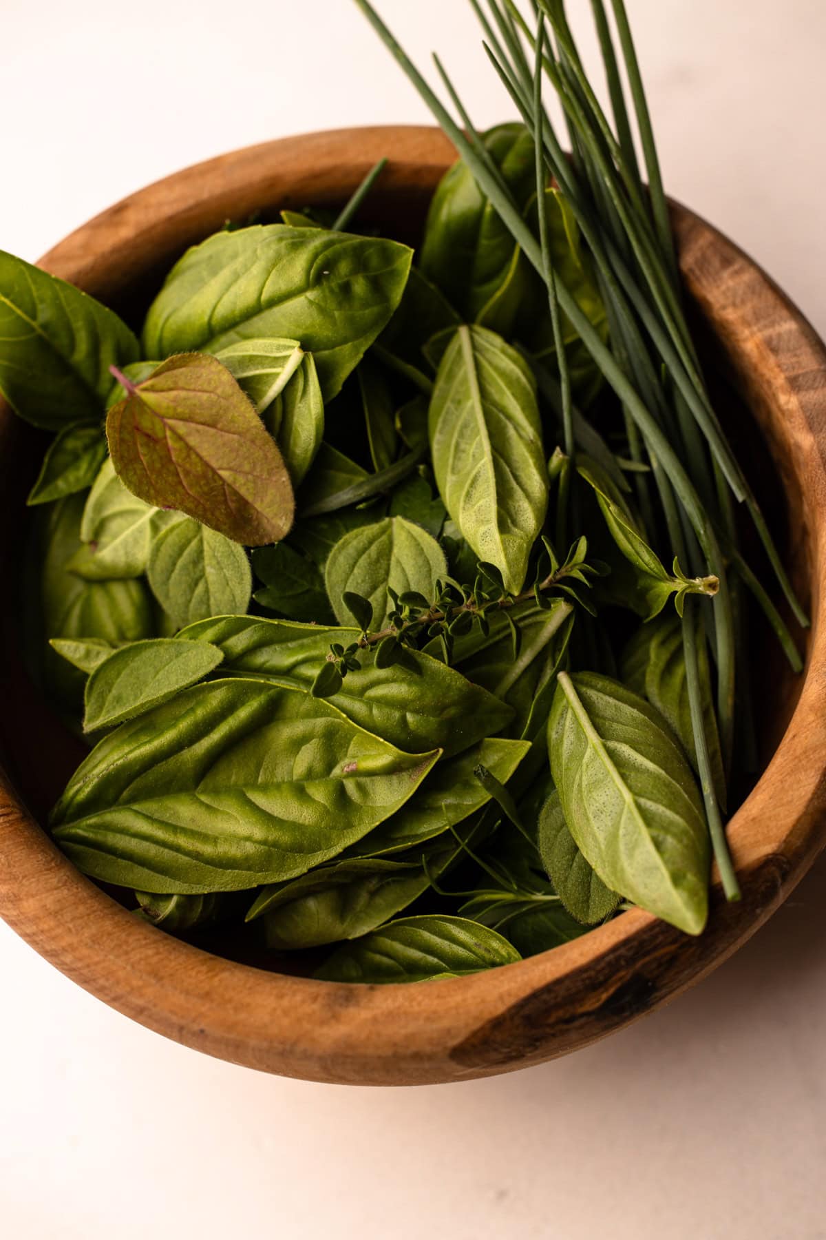 Fresh basil and chives and other herbs in a wooden bowl.