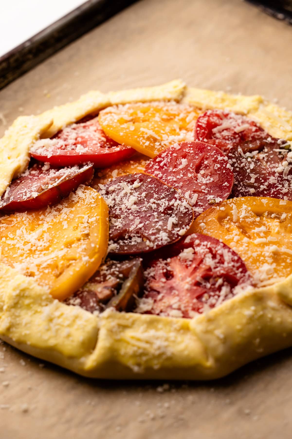 A tomato galette being prepared with heirloom tomato slices and a sprinkle of cheese.