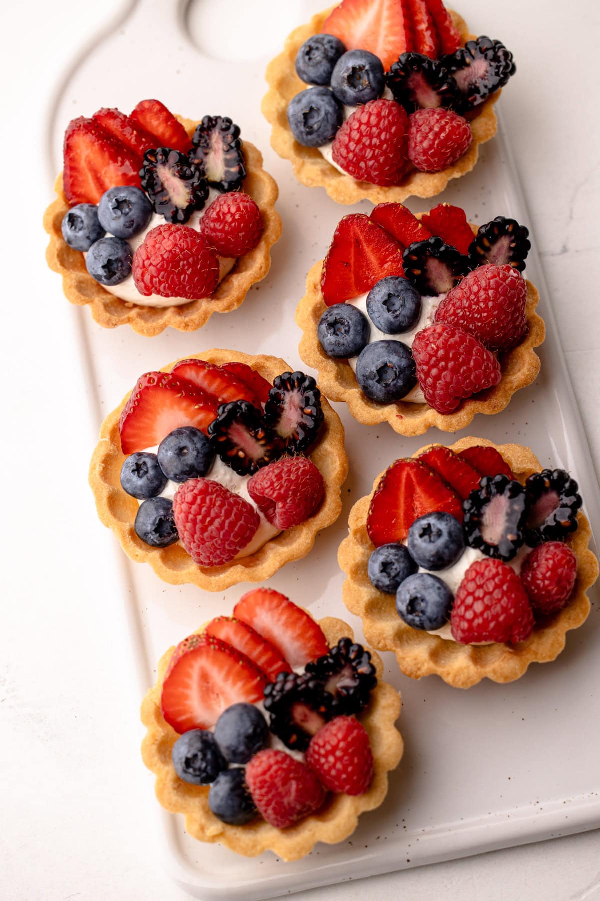 A white platter with several mini fruit tarts, each topped with different berries.