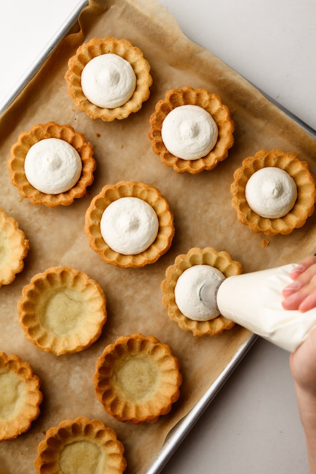 Piping a whipped cream filling into baked mini fruit tarts.