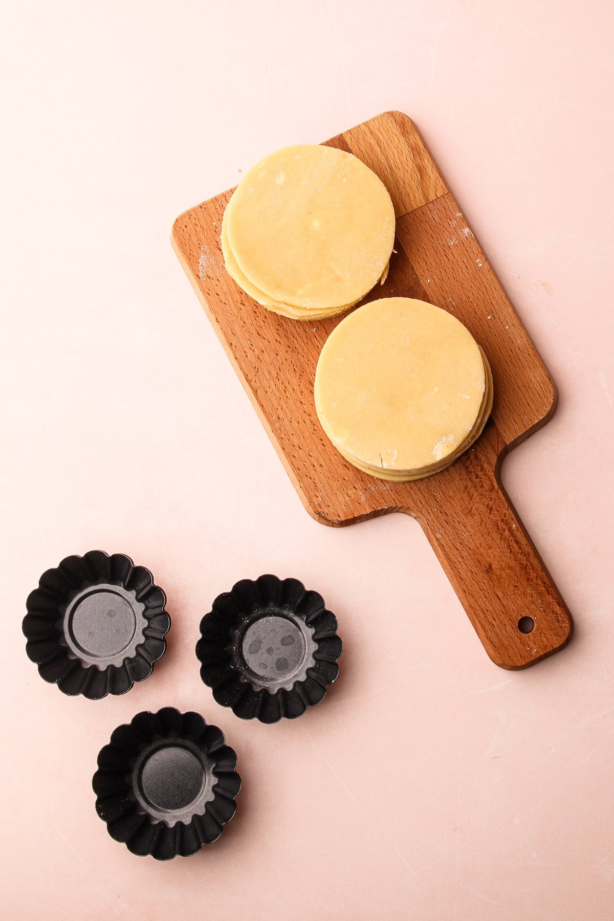 Cutting board with rounds of dough ready to be pressed into molds for mini fruit tarts.