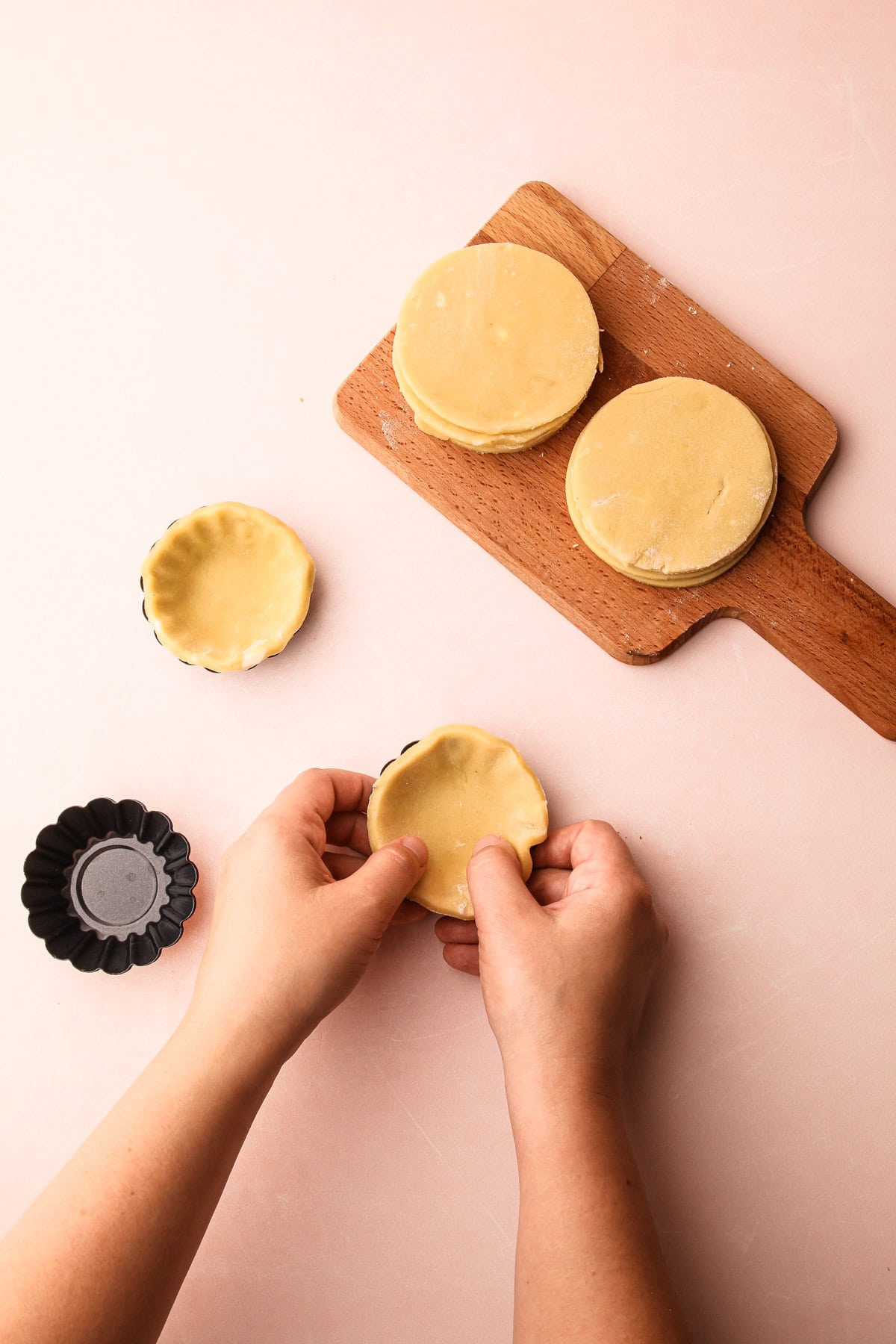 Dough being pressed into molds to form shells for fruit tartlets.