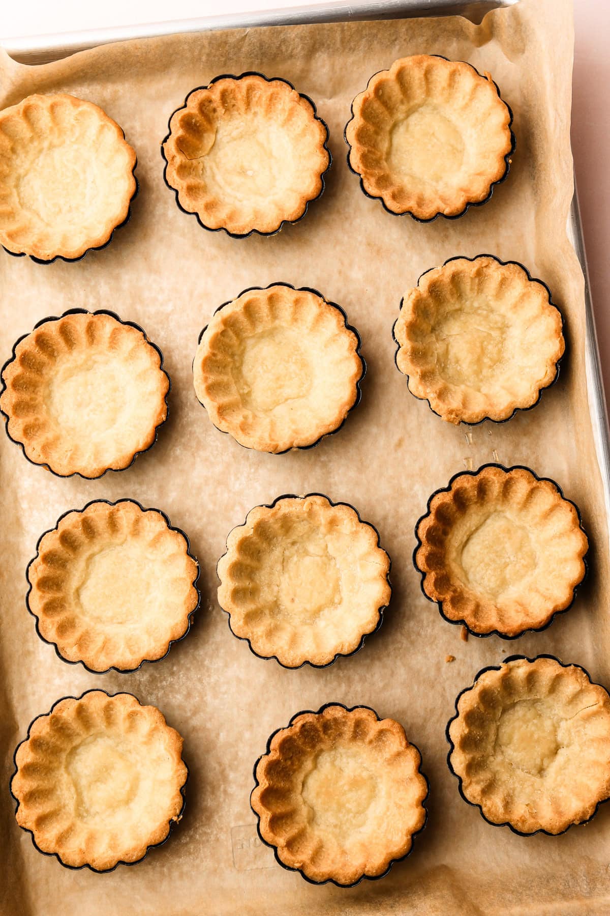 Empty baked tart shells on a baking sheet.