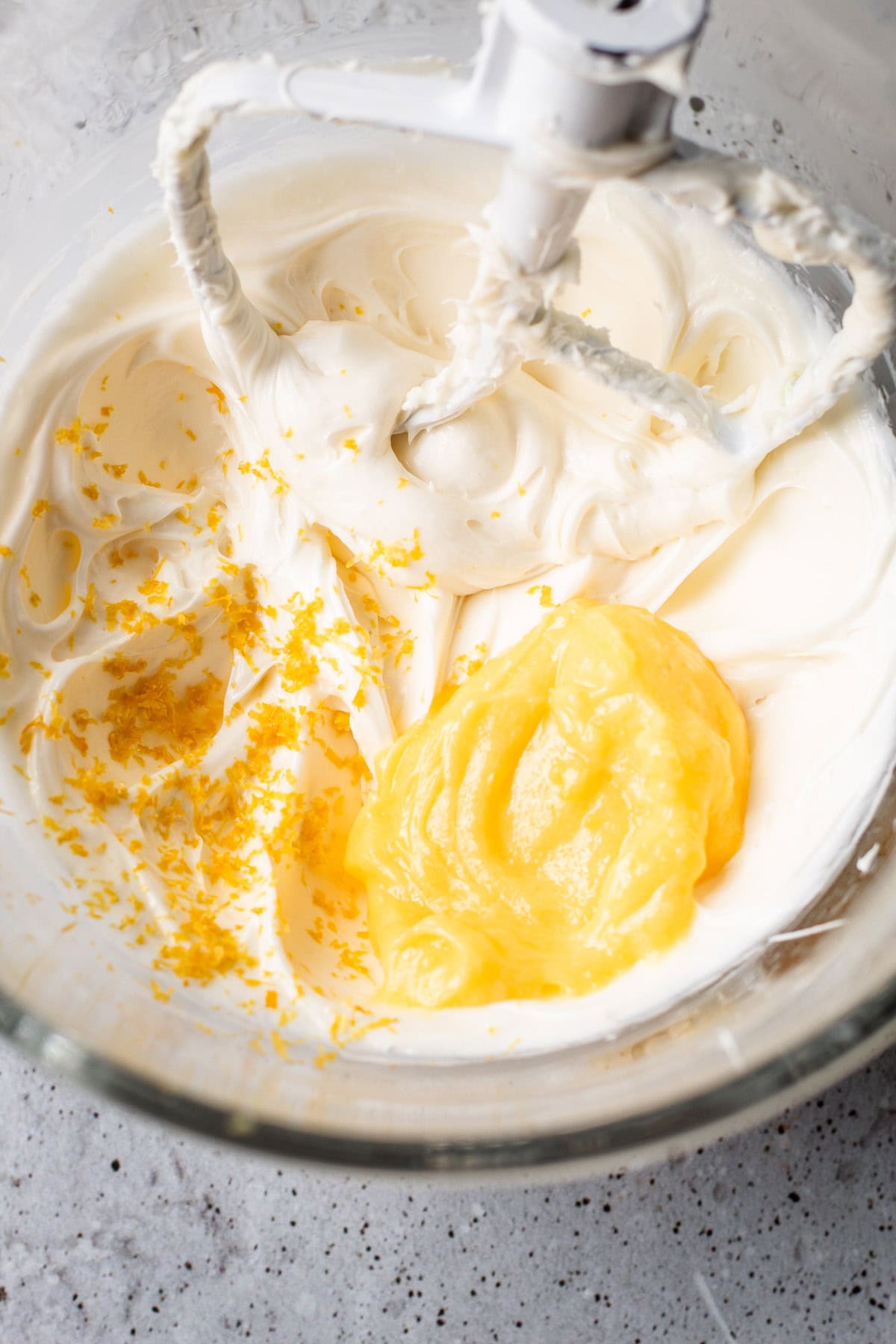 Lemon curd and zest added to whipped cream in a glass mixing bowl.