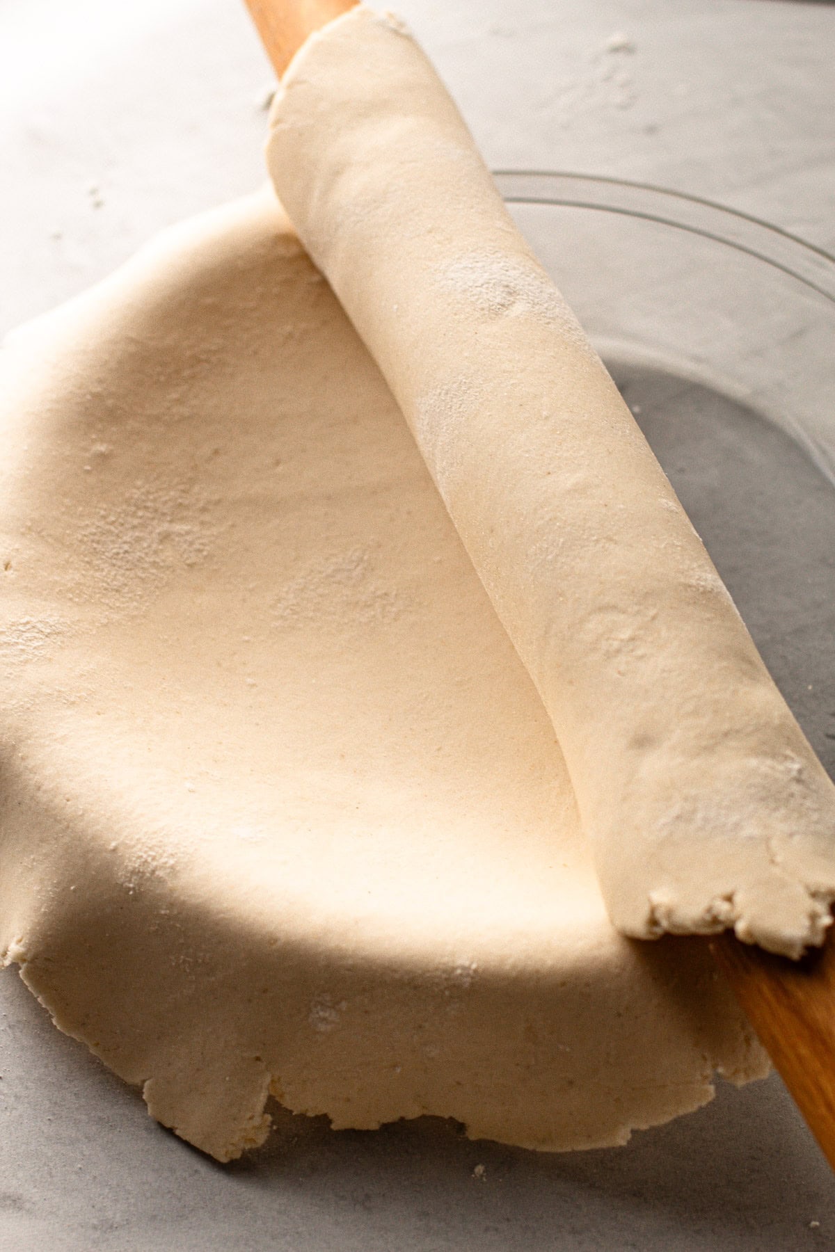 A rolling pin with gluten free pie dough wrapped around it draped over a pie plate.