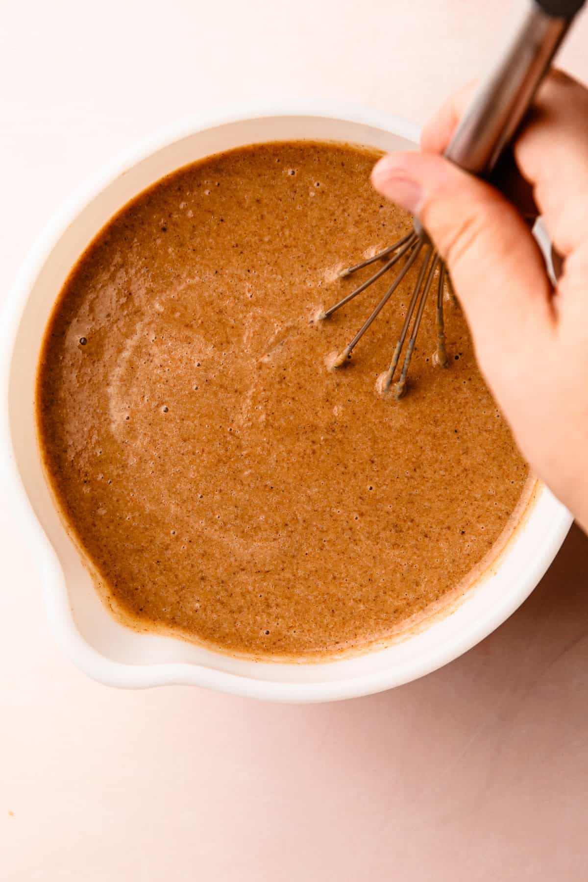 Whisking a rich, spiced batter for an apple butter pie in a white mixing bowl.