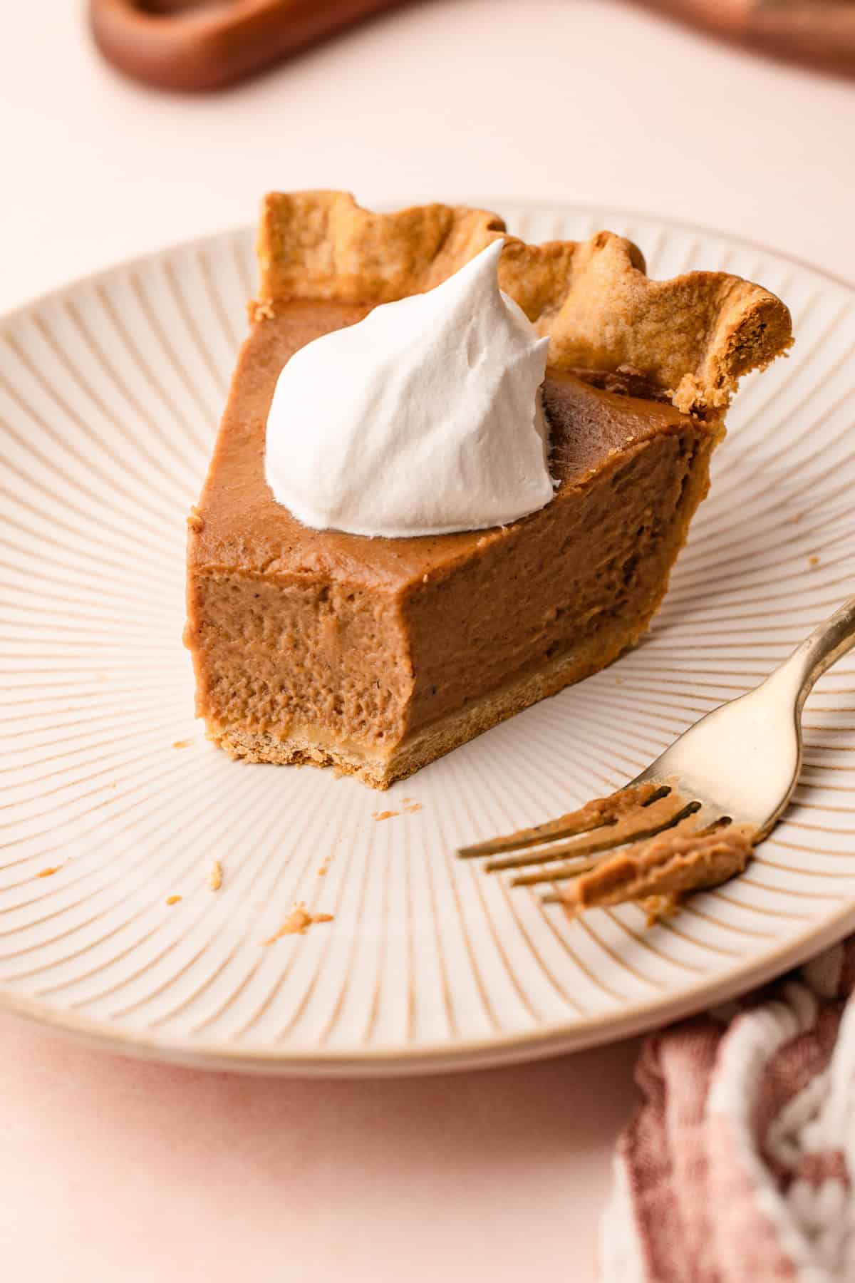 A slice of apple butter pie with a bite taken out, revealing the silky interior, topped with a dollop of whipped cream.