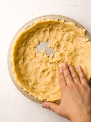 Hands pressing in the pie crust to a baking tin.