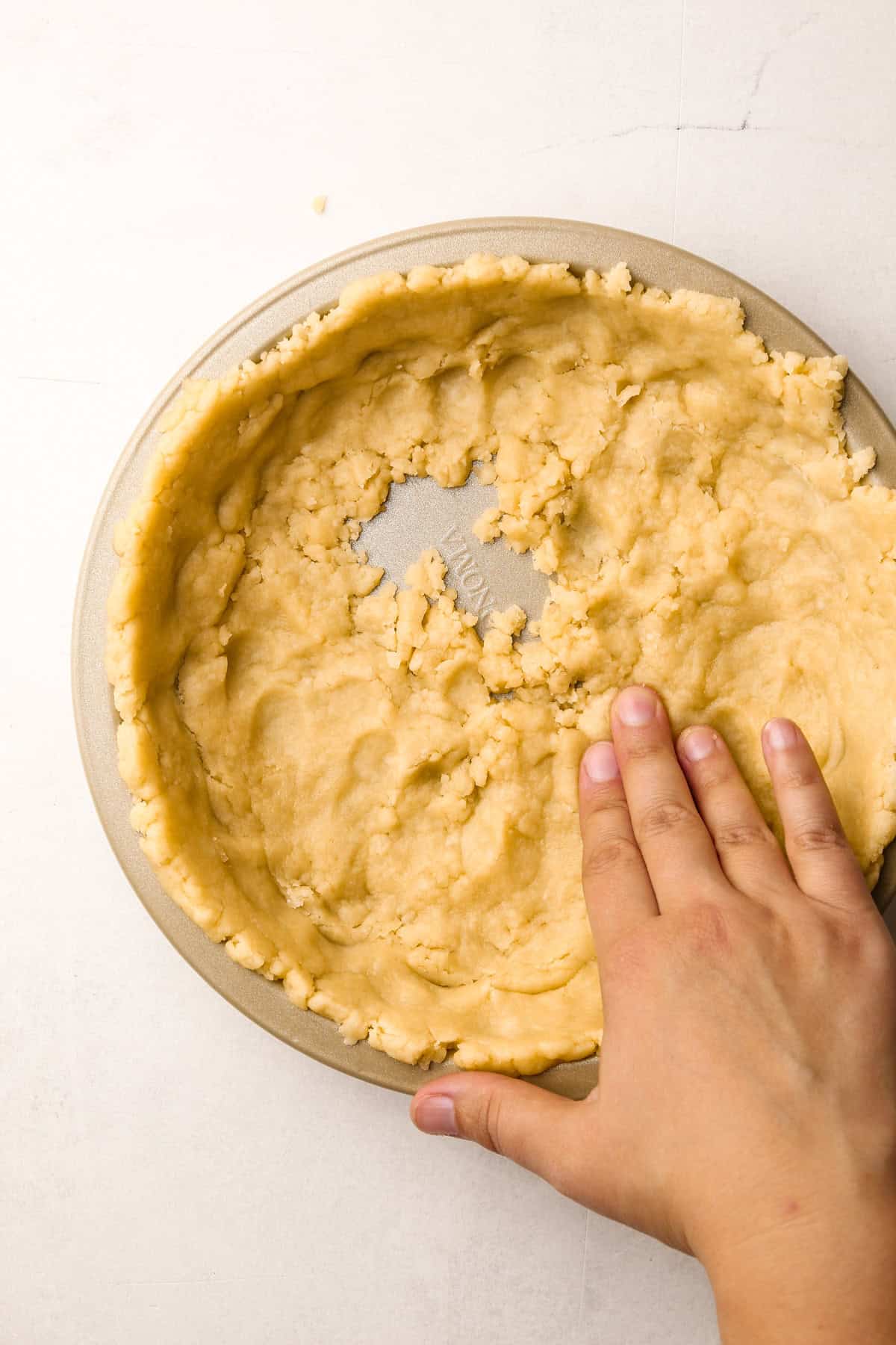 Hands pressing in the pie crust to a baking tin.