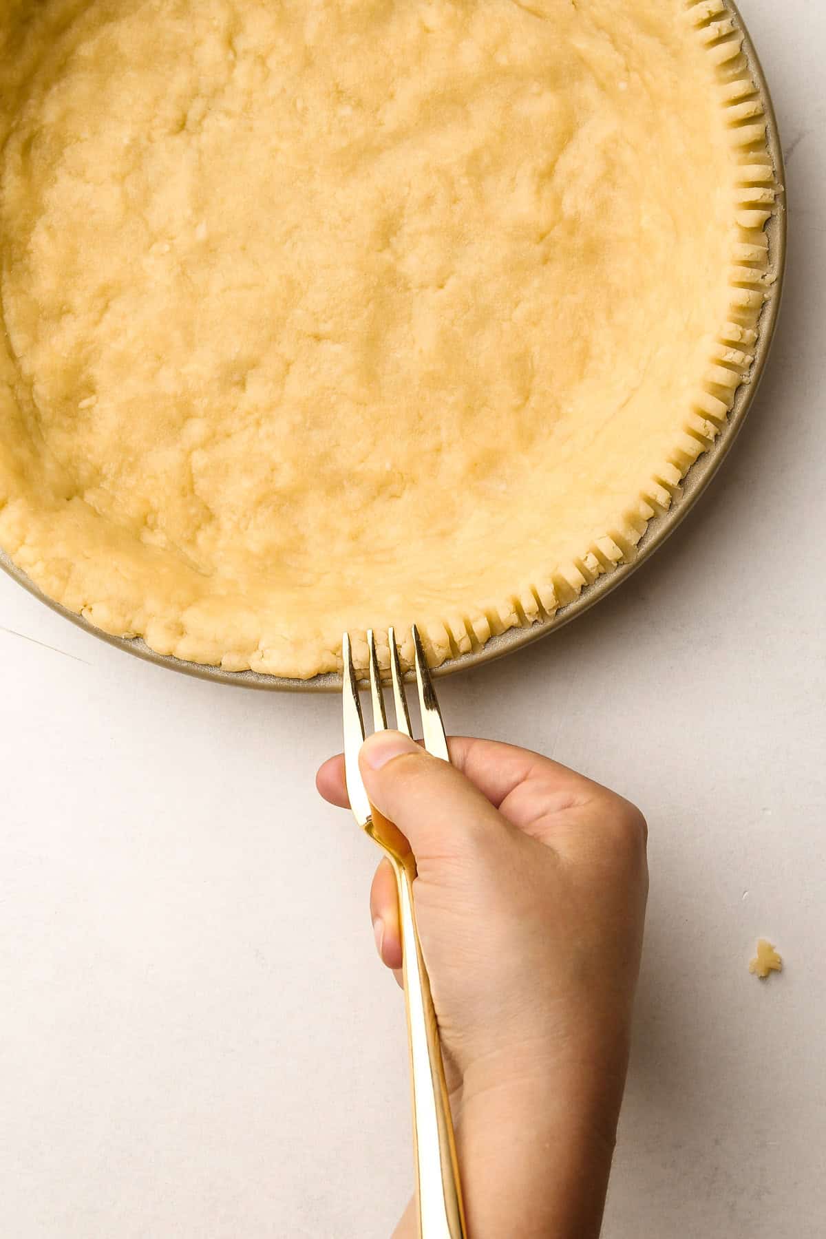 A fork making a decorative edge on a melted butter pie crust.