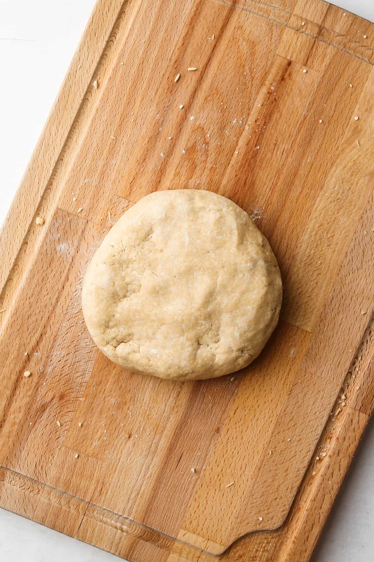 A whole wheat pie dough disk on a wooden board.