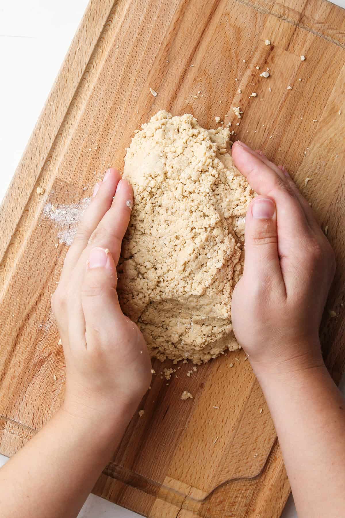 Two hands shaping together whole wheat pie dough.