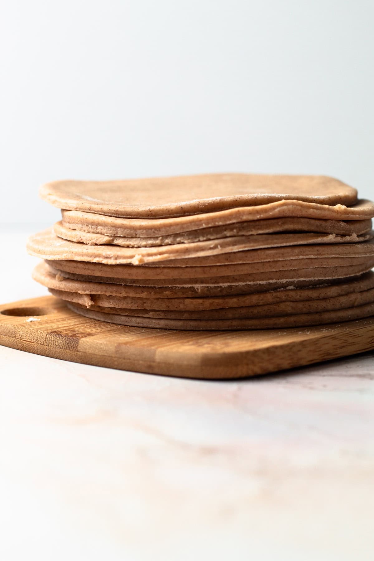 Stack of rolled pumpkin pasty dough on a wooden board.