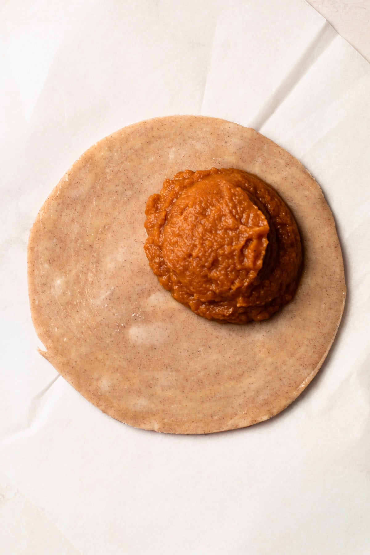 Pumpkin pasty dough with a scoop of pumpkin filling in the center.