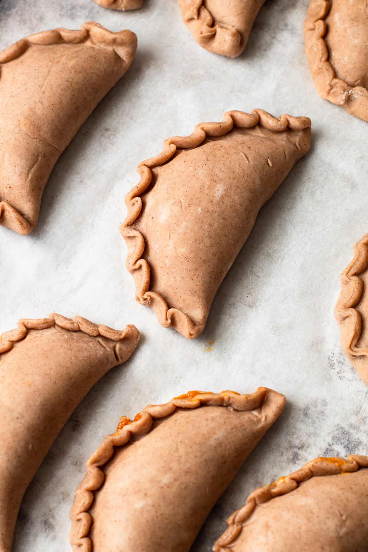 Unbaked pumpkin pasties on a baking tray.