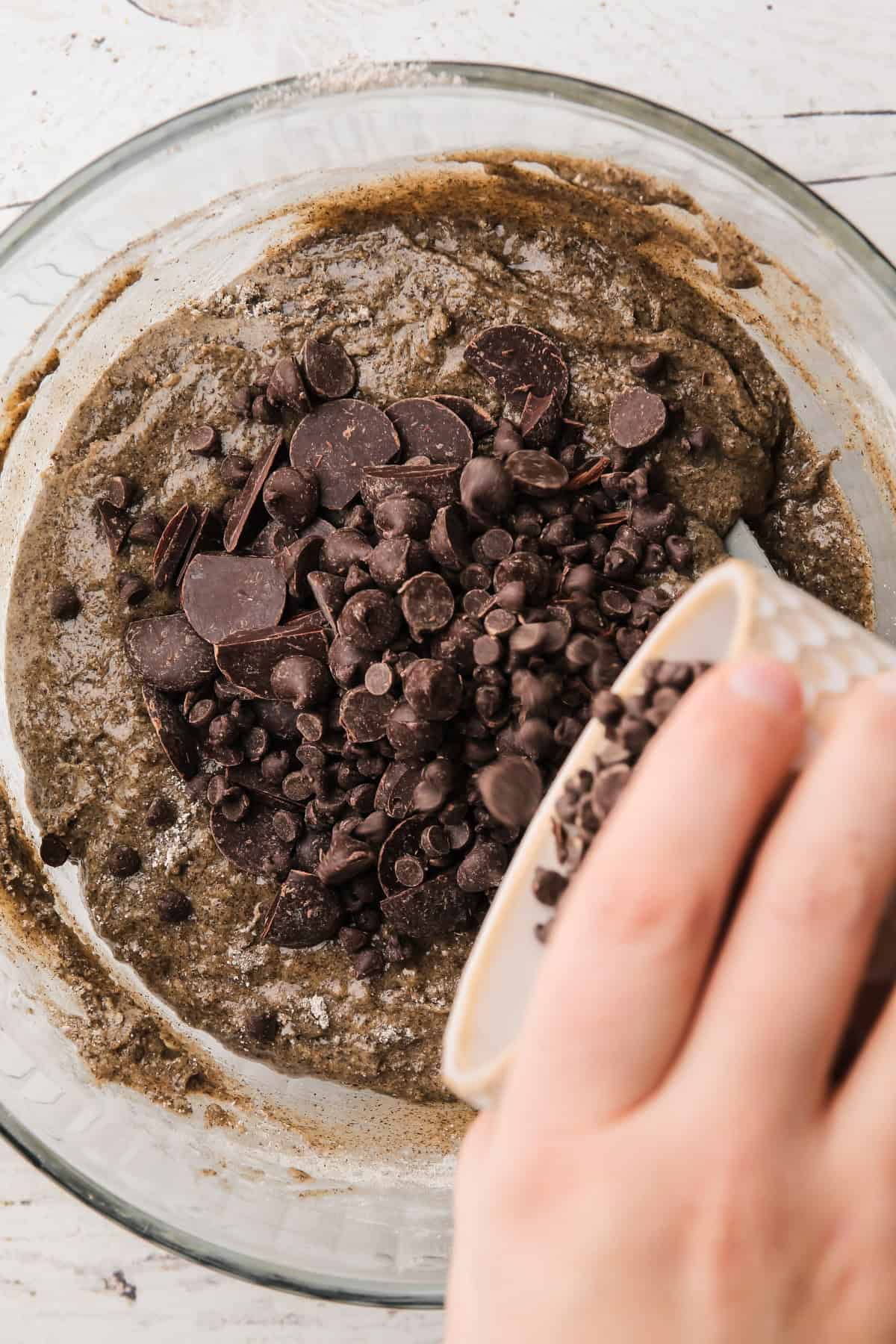 Chocolate chips being poured into the cookie dough for buckwheat chocolate chip cookies.