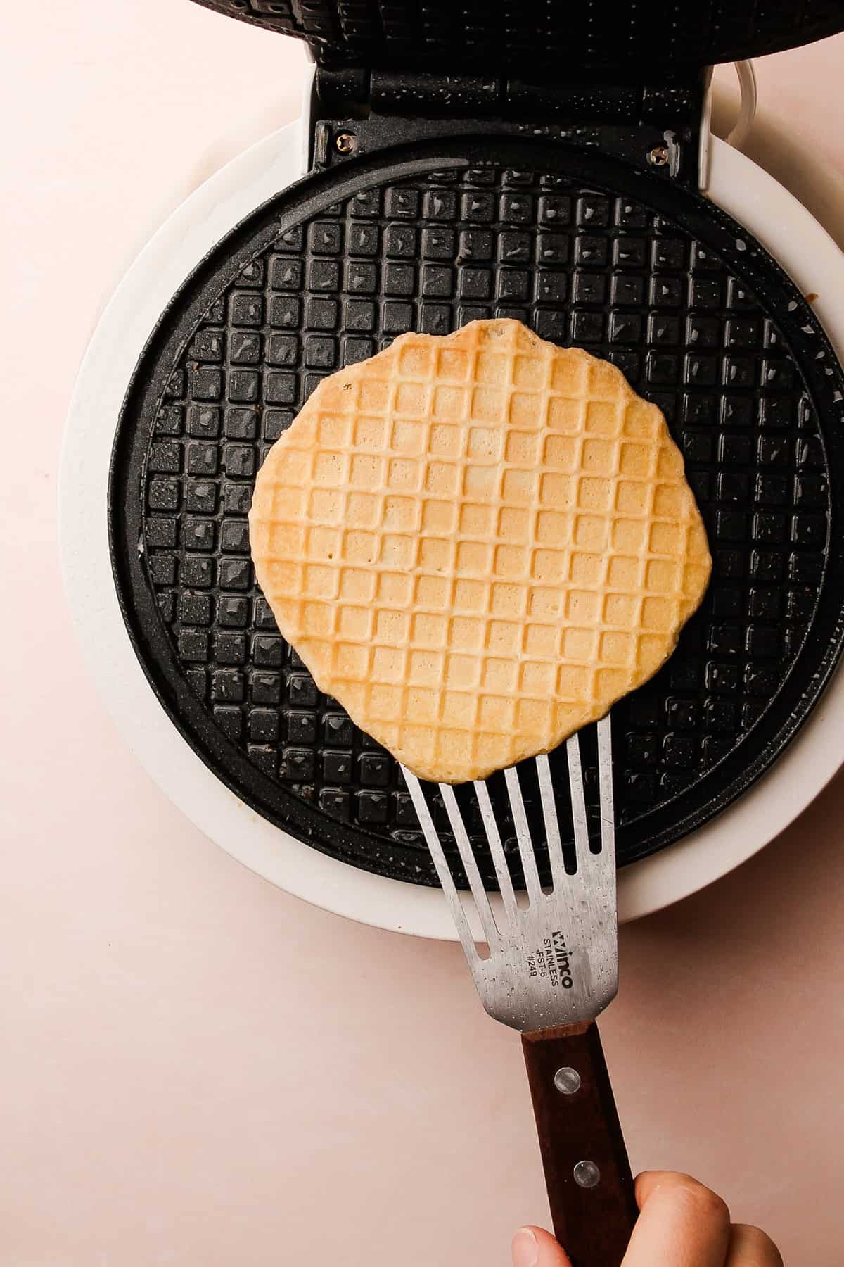 A spatula lifting a warm pizzelle off the iron, revealing its delicate pattern.