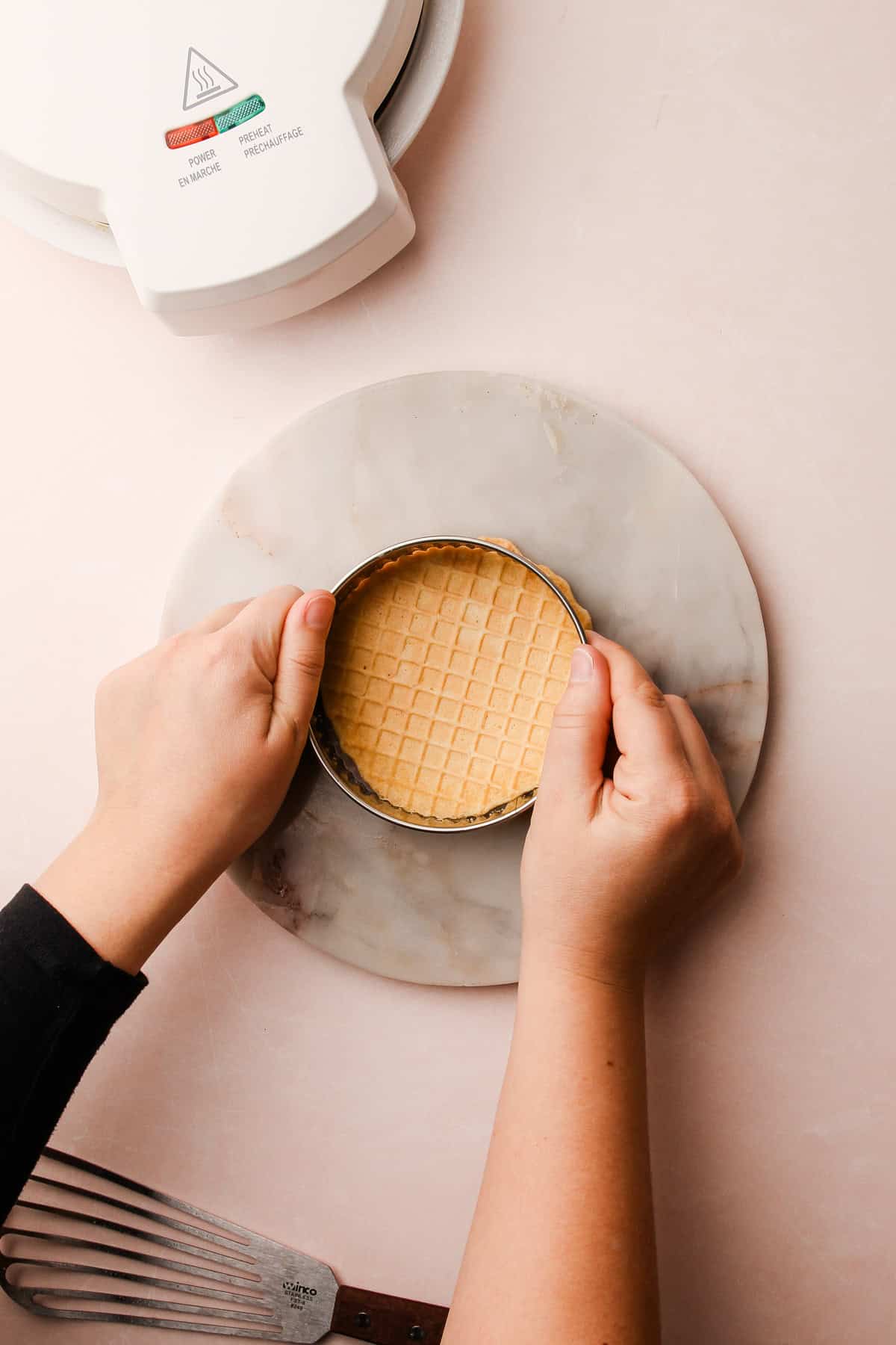 A single pizzelle on a marble surface, ready to be trimmed for an even shape.