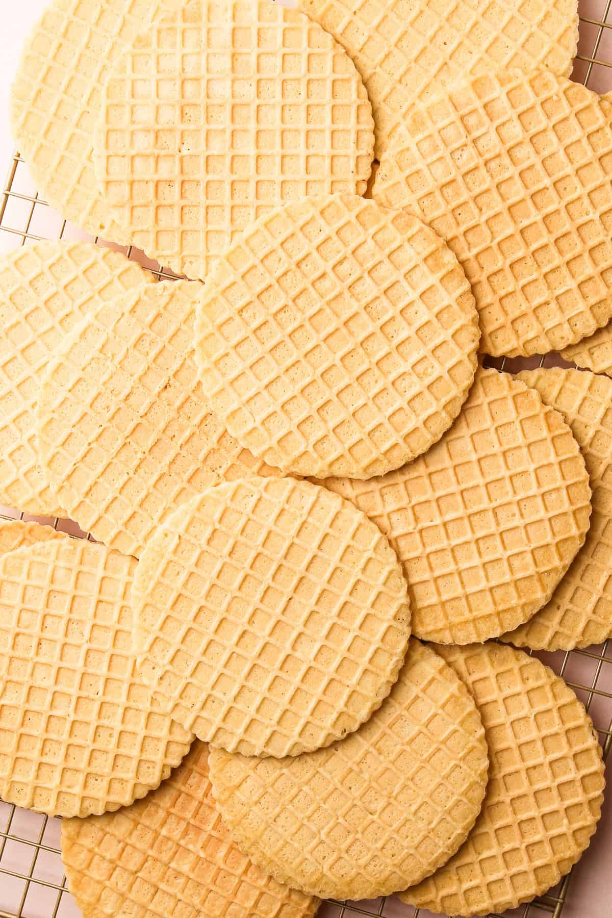 A cooling rack filled with golden brown pizzelles, stacked slightly overlapping.