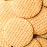 A cooling rack filled with golden brown pizzelles, stacked slightly overlapping.