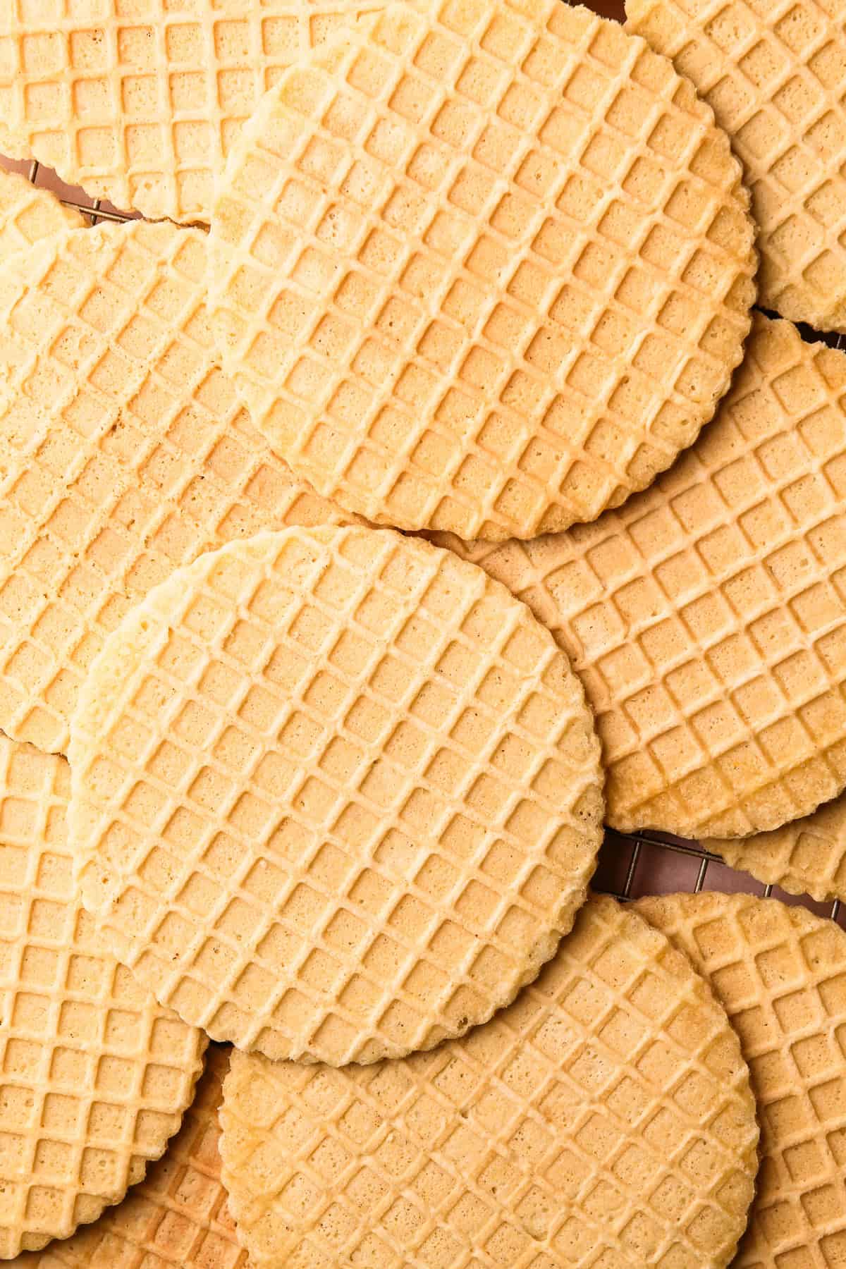 A cooling rack filled with golden brown pizzelles, stacked slightly overlapping.