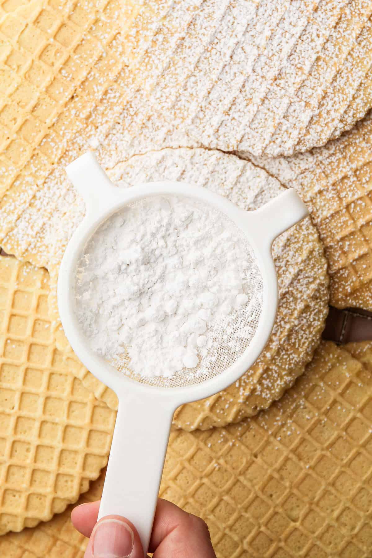 A sifter filled with powdered sugar, ready to dust freshly made pizzelles.