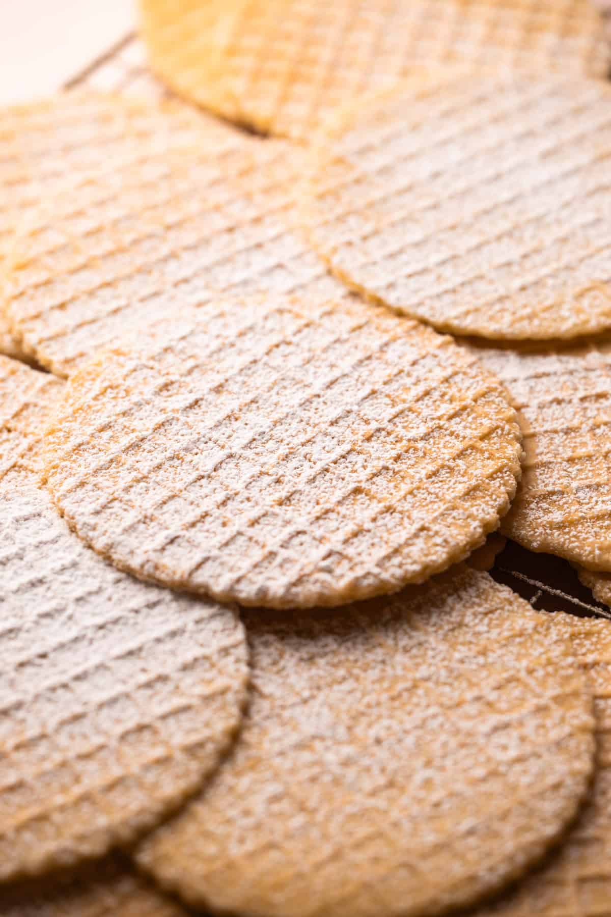 A batch of pizzelle cookies dusted with powdered sugar on a cooling rack.