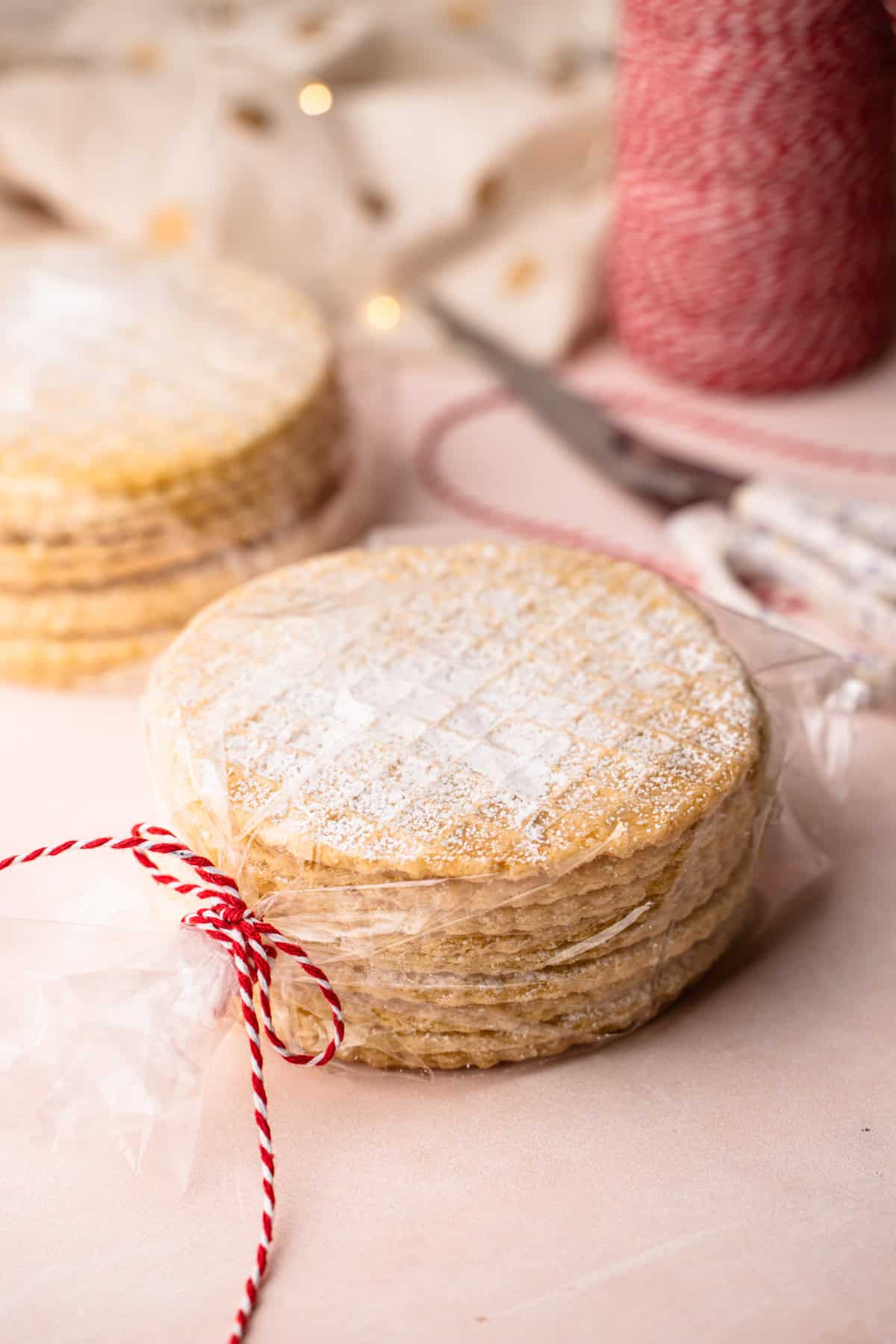 A stack of homemade pizzelles wrapped in clear plastic and tied with red and white twine.