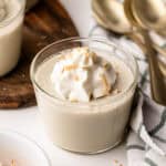A serving of coconut milk pudding with whipped cream on top, surrounded by gold spoons and a dish towel.