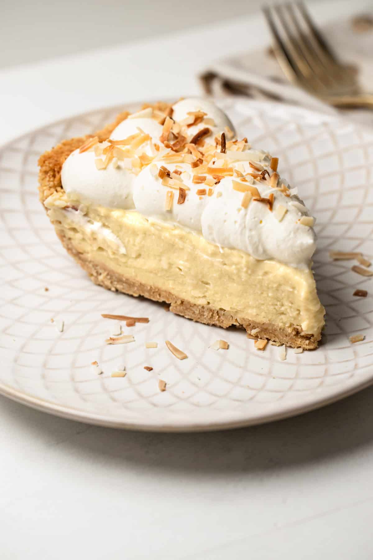 Close-up of a slice of coconut pudding pie on a plate with golden toasted coconut garnish.