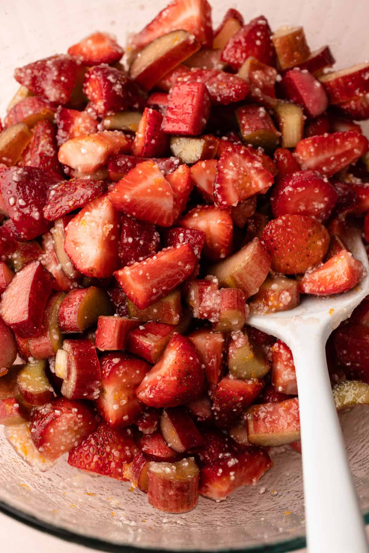 Strawberries and rhubarb cut up in a bowl with ingredients to make pie filling.