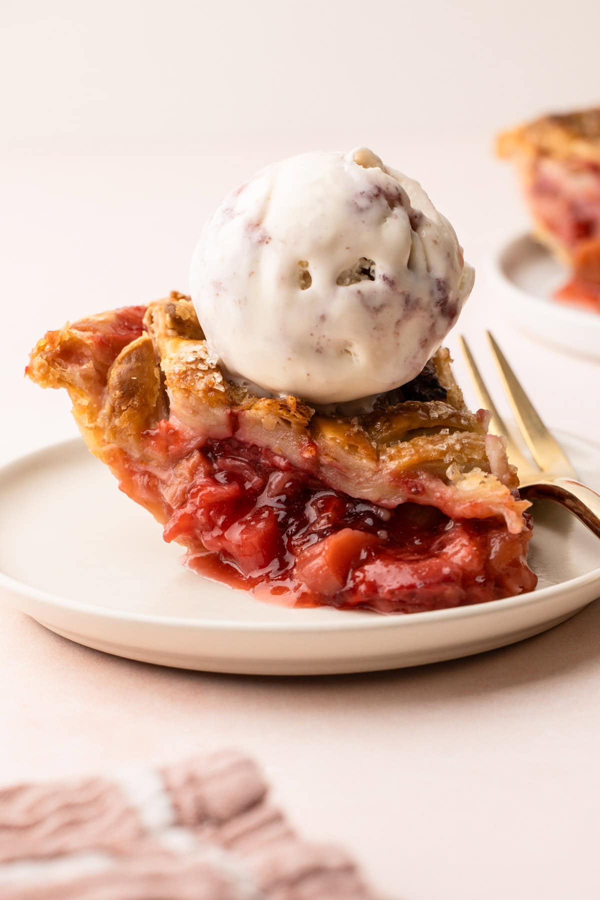 A slice of prepared strawberry rhubarb pie with a scoop of ice cream on top.