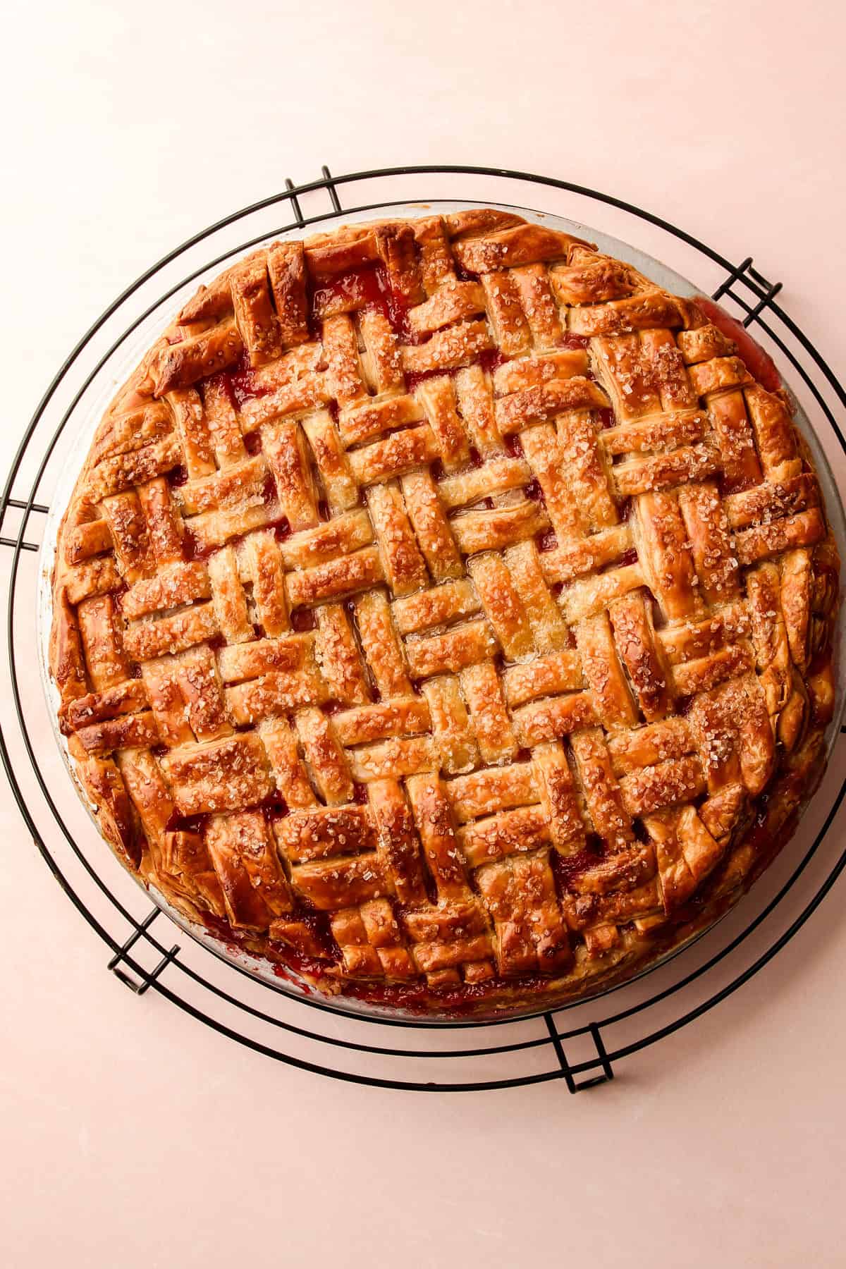 A baked strawberry rhubarb pie cooling on a pie rack.